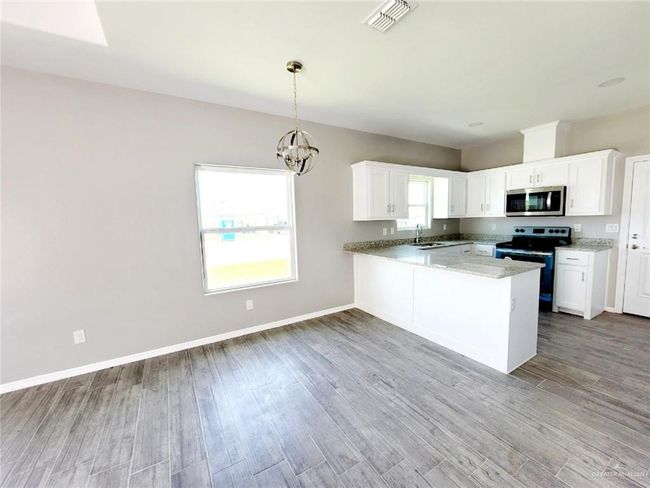 Kitchen featuring stainless steel microwave, electric range oven, light wood-style floors, a peninsula, and white cabinetry | Image 4