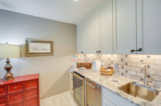 Kitchen with wine cooler, decorative backsplash, light stone countertops, and white cabinetry | Image 8