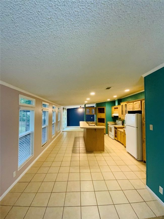 Kitchen with crown molding, a textured ceiling, open floor plan, white appliances, and a kitchen island | Image 7
