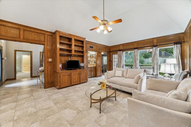This view of the room includes moves from the entry, built-ins, and wet bar to the left, and a bank of large windows on the far wall, which overlook the pool and butterfly garden. | Image 5