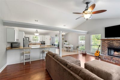 Living room with a brick fireplace, ceiling fan, wood-type flooring, lofted ceiling, and sink | Image 3