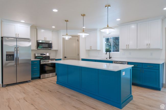 Kitchen featuring stainless steel appliances, blue cabinetry, a sink, a kitchen island, and light countertops | Image 11