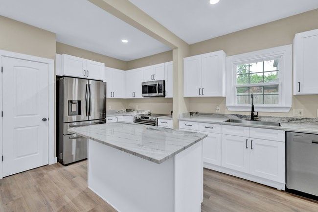 Kitchen with light stone countertops, a sink, a center island, white cabinets, and appliances with stainless steel finishes | Image 10