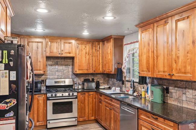 Kitchen featuring dark stone countertops, a sink, appliances with stainless steel finishes, and decorative backsplash | Image 10