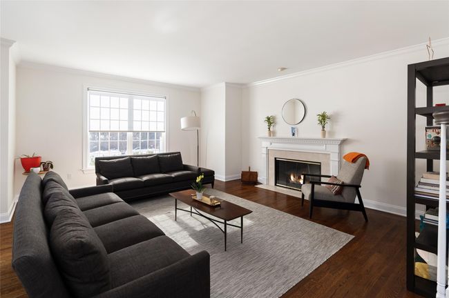Large living room with multiple windows and dark hardwood floors, wood burning fireplace and crown molding | Image 5