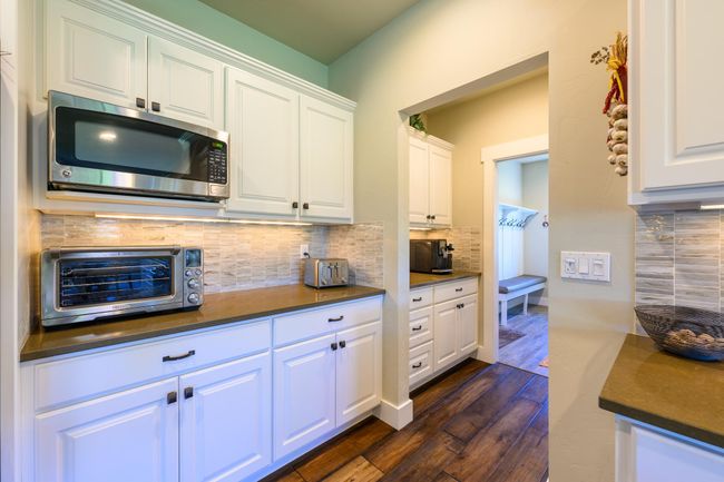 Kitchen with stainless steel microwave, dark countertops, dark wood finished floors, tasteful backsplash, and white cabinets | Image 16