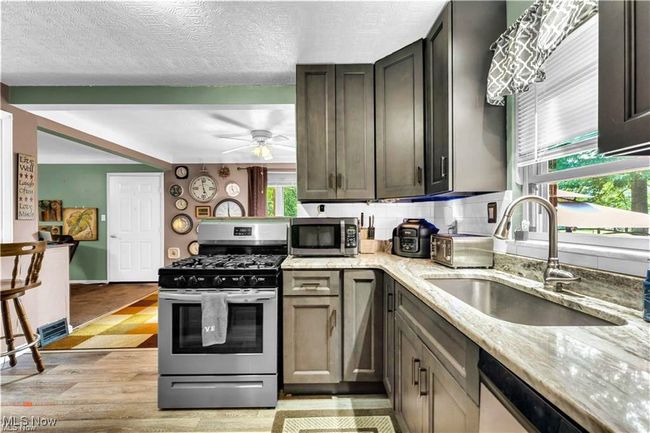 Kitchen with stainless steel appliances, a sink, light stone counters, a ceiling fan, and light wood-style flooring | Image 15