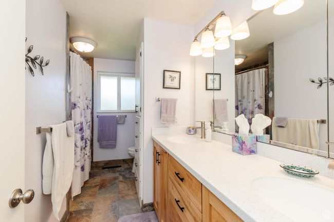 Bathroom with toilet, stone finish floor, a sink, and double vanity | Image 16