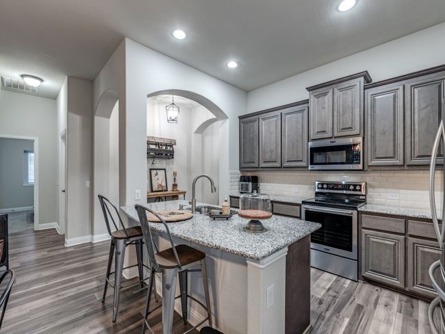 Kitchen featuring light stone counters, a center island with sink, appliances with stainless steel finishes, dark hardwood / wood-style flooring, and decorative backsplash | Image 15