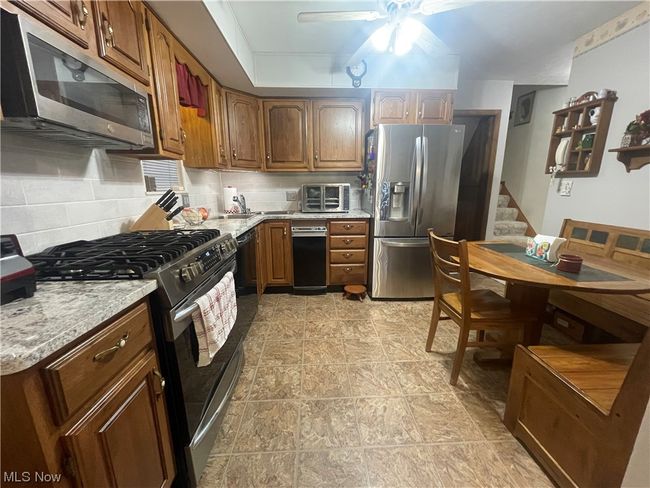 Kitchen with light stone countertops, tasteful backsplash, appliances with stainless steel finishes, light tile floors, and ceiling fan | Image 12