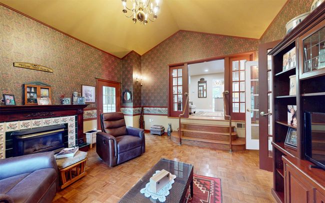 Living room featuring lofted ceiling, wallpapered walls, a chandelier, wainscoting, and a tile fireplace | Image 24