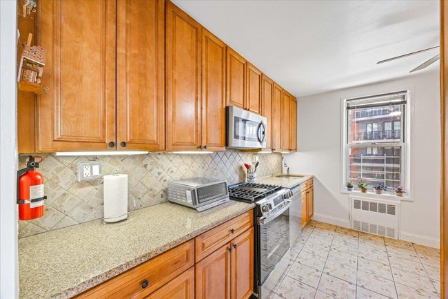 Kitchen featuring radiator, appliances with stainless steel finishes, a sink, baseboards, and tasteful backsplash | Image 4