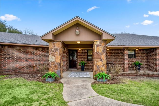 Doorway to property featuring stone siding, brick siding, and roof with shingles | Image 4