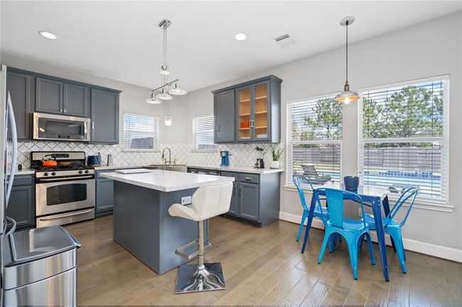 Bright and modern kitchen with sleek dark cabinets, stainless steel appliances, and a central island. The dining area features a chic table with blue chairs, and large windows provide natural light and a view of the backyard with a pool. | Image 29