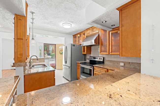Kitchen with appliances with stainless steel finishes, exhaust hood, brown cabinets, a textured ceiling, and light stone counters | Image 11