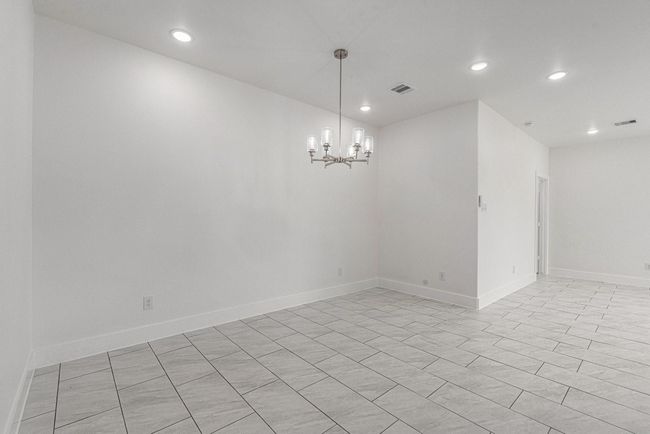 Bright, modern dining area with white walls and tiled flooring. Features recessed lighting and a contemporary chandelier. Open layout with a minimalist aesthetic. | Image 17