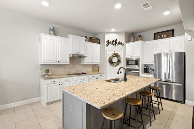 Kitchen with appliances with stainless steel finishes, a kitchen island with sink, and white cabinetry | Image 15