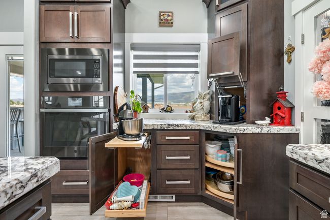 Kitchen featuring oven, stainless steel microwave, dark brown cabinetry, and light stone counters | Image 30