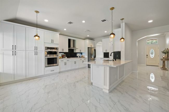 Kitchen w/breakfast space, stainless steel appliances, wall chimney exhaust hood, white cabinets, and recessed lighting | Image 9