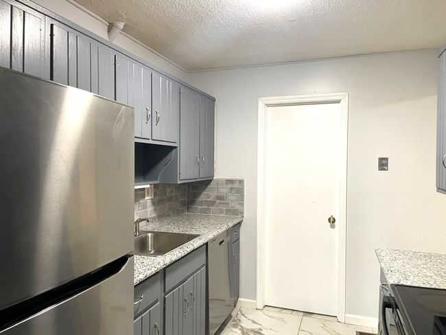 Kitchen with stainless steel appliances, gray cabinetry, decorative backsplash, light marble finish flooring, and a textured ceiling | Image 5