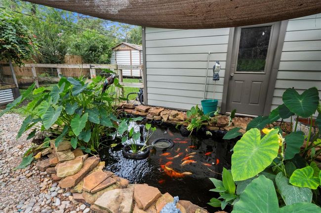 This backyard photo showcases a charming koi pond surrounded by lush greenery and stone edging. The area is well-maintained with a shaded canopy, creating a serene outdoor retreat next to the outdoor area with light siding and a door leading inside the garage. Ideal for nature lovers seeking a peaceful home garden feature. | Image 43