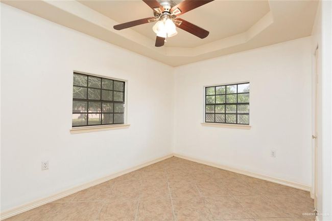 Tiled empty room with a tray ceiling, baseboards, and ceiling fan | Image 9