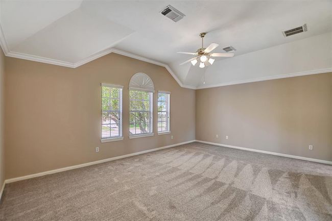 This spacious room features neutral walls, carpeted flooring, and a vaulted ceiling with a ceiling fan. Large windows with decorative trim provide ample natural light. | Image 32