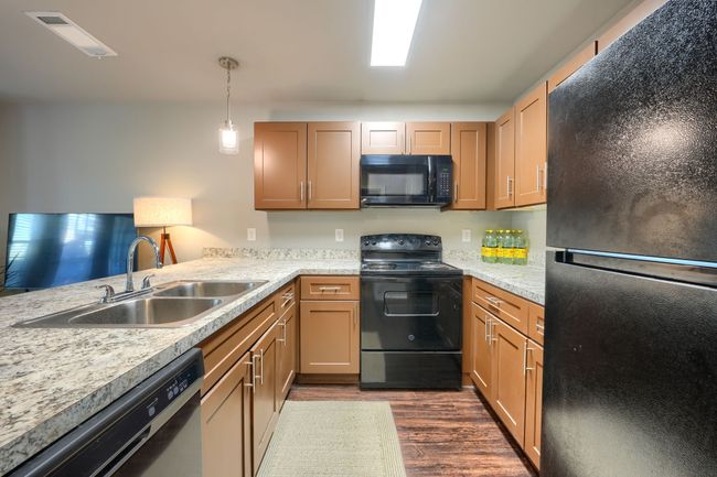 Kitchen featuring dark wood-style flooring, a sink, hanging light fixtures, black appliances, and light countertops | Image 10