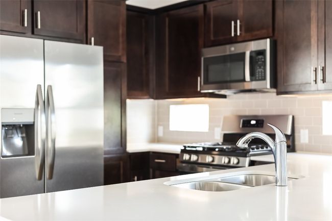 Kitchen featuring stainless steel appliances, decorative backsplash, light countertops, and dark brown cabinetry | Image 13