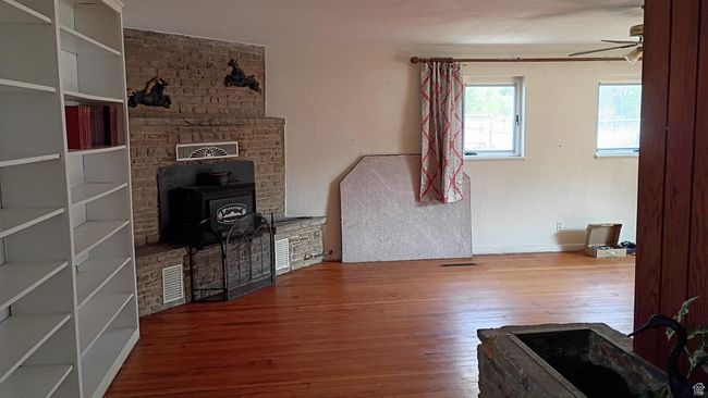 Family room with a wood stove, hardwood / wood-style flooring and ceiling fan. | Image 31