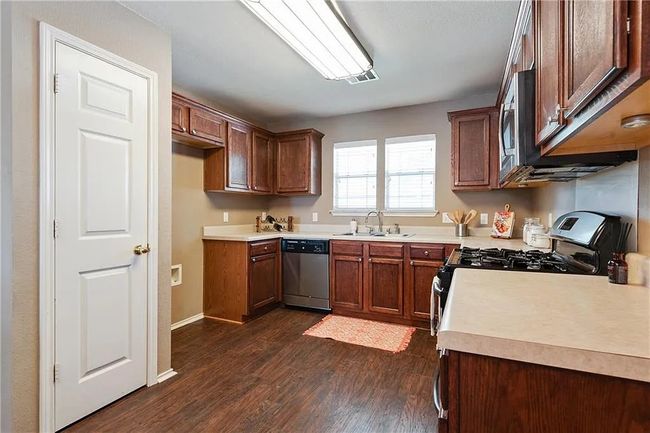 Kitchen featuring stainless steel appliances, a sink, dark wood-style floors, light countertops, and baseboards | Image 6