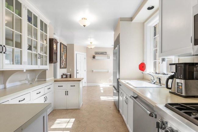 Kitchen with appliances with stainless steel finishes, glass insert cabinets, white cabinetry, a sink, and baseboards | Image 10