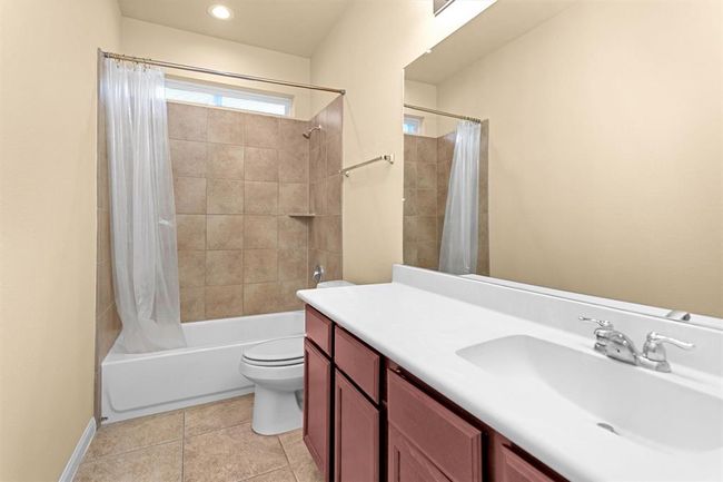 The secondary full bathroom is both functional and stylish, featuring a large vanity with ample cabinet and drawer storage. A large framed mirror sits above the vanity, complemented by overhead lighting. A tub and shower combo is surrounded by classic tile, with a transom window above. | Image 19
