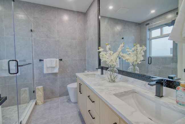 Bathroom with double vanity, a shower stall, tile patterned floors, toilet, and tile walls | Image 13