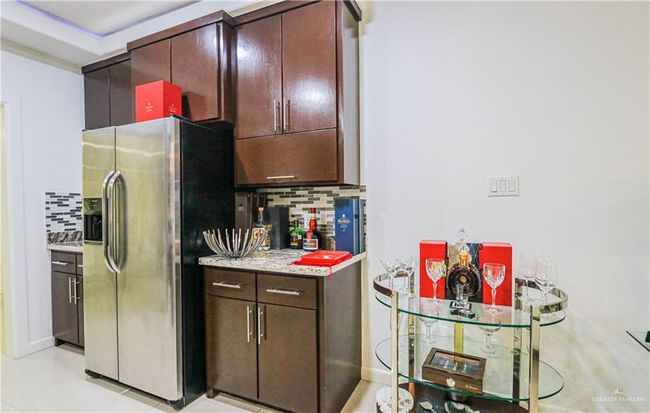 Kitchen with dark brown cabinets, stainless steel fridge with ice dispenser, light tile patterned floors, and tasteful backsplash | Image 11