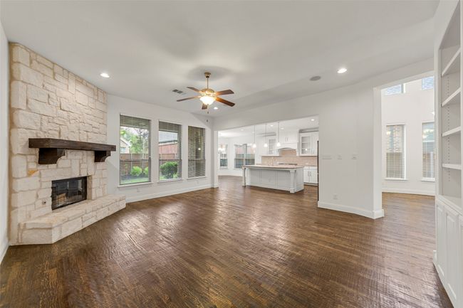 Unfurnished living room with a ceiling fan, a stone fireplace, visible vents, baseboards, and dark wood-type flooring | Image 15