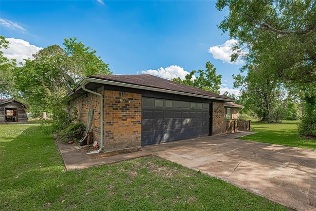 Charming brick home with a two-car garage set amidst lush greenery. The spacious driveway and mature trees enhance the property’s curb appeal, offering a serene and private atmosphere. | Image 33