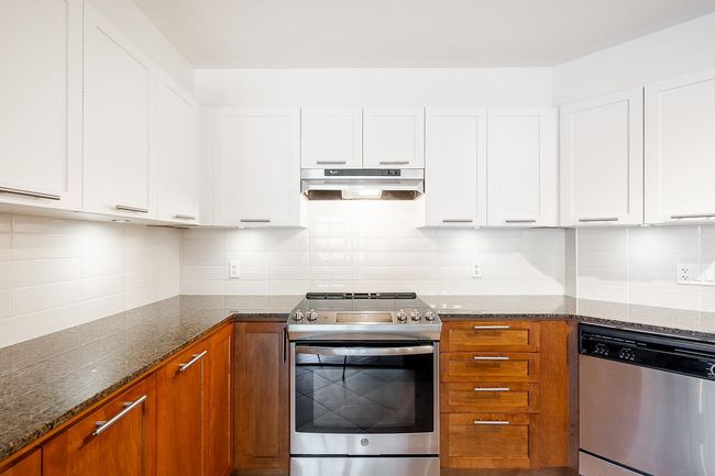 Kitchen featuring appliances with stainless steel finishes, white cabinets, dark stone countertops, and under cabinet range hood | Image 5