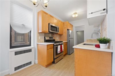 Kitchen with sink, radiator heating unit, backsplash, stainless steel appliances, and light wood-type flooring, Quartz counter tops, matching backsplash, 2 tall windows allowing lots of natural light | Image 2