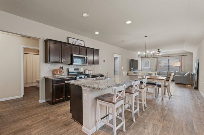 Kitchen featuring stainless steel appliances, dark brown cabinetry, open floor plan, wood finished floors, and a breakfast bar | Image 5