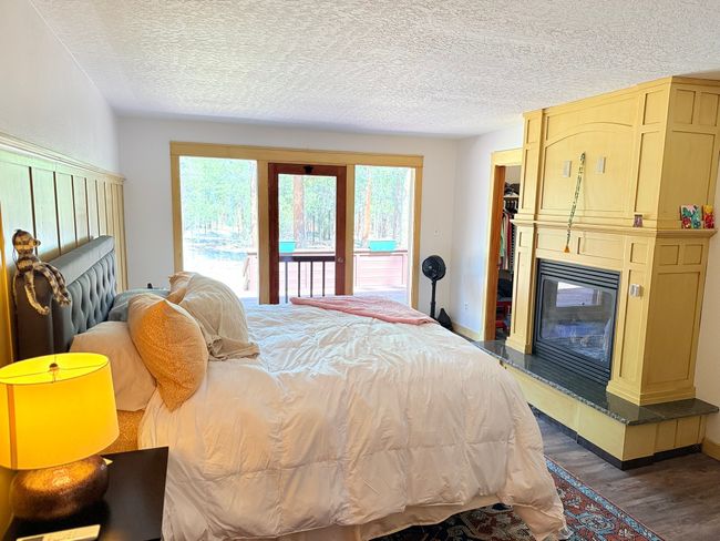Bedroom featuring a textured ceiling, baseboards, wood finished floors, access to exterior, and a glass covered gas fireplace | Image 33