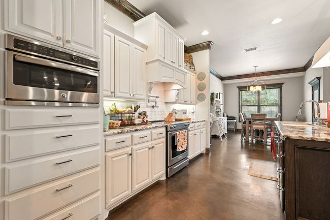 Kitchen with appliances with stainless steel finishes, crown molding, decorative backsplash, finished concrete flooring, and light stone counters | Image 7