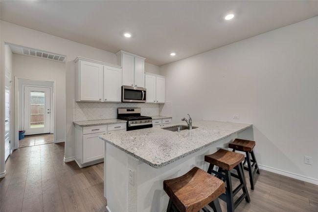 Kitchen featuring appliances with stainless steel finishes, dark wood-style floors, a sink, a peninsula, and white cabinetry | Image 18