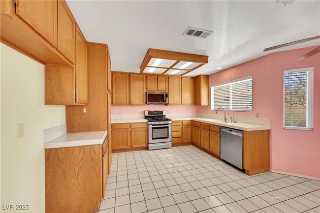 Kitchen featuring light countertops, visible vents, appliances with stainless steel finishes, a ceiling fan, and a sink | Image 11