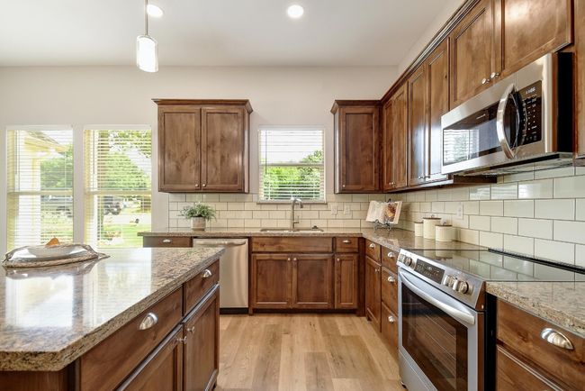 Kitchen with stainless steel appliances, light wood finished floors, backsplash, light stone countertops, and recessed lighting | Image 12