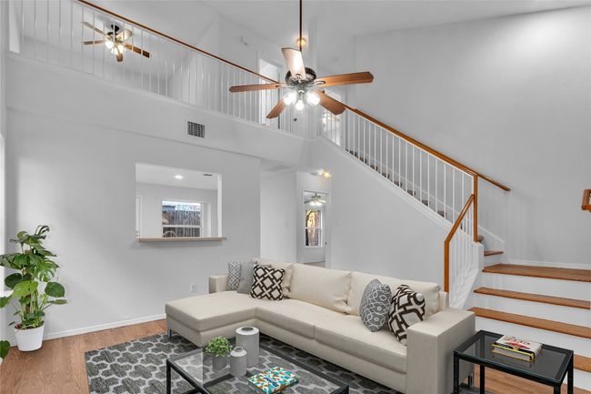 Living room with a ceiling fan, wood finished floors, stairs, and a high ceiling | Image 4