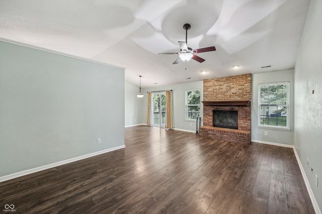 unfurnished living room with ceiling fan, dark wood finished floors, a fireplace, and lofted ceiling | Image 5