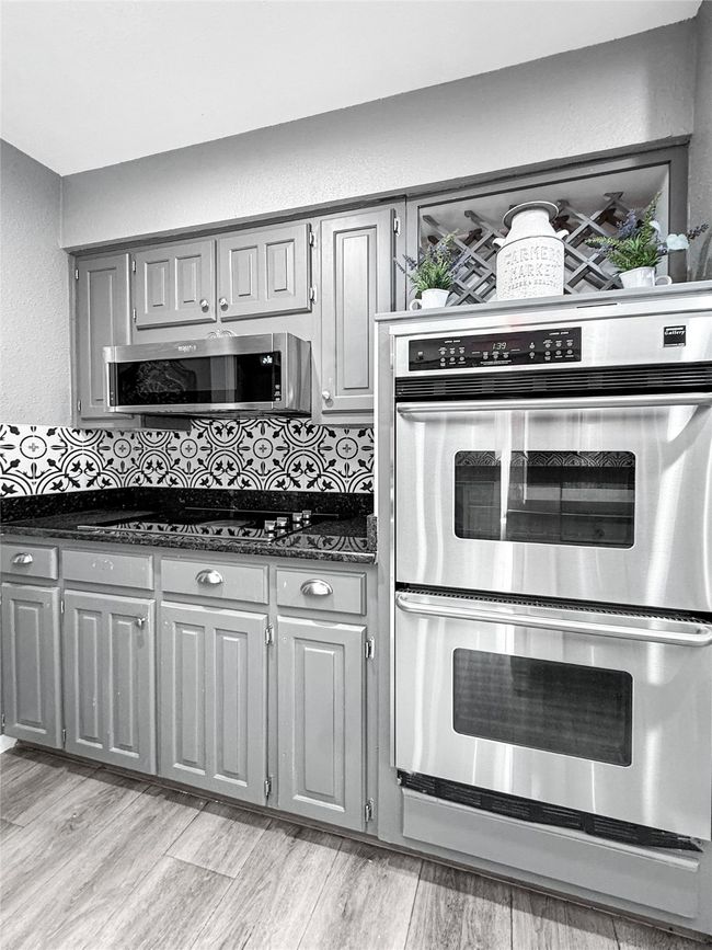 Kitchen with gray cabinets, stainless steel appliances, a textured wall, light wood-style flooring, and dark stone counters | Image 15