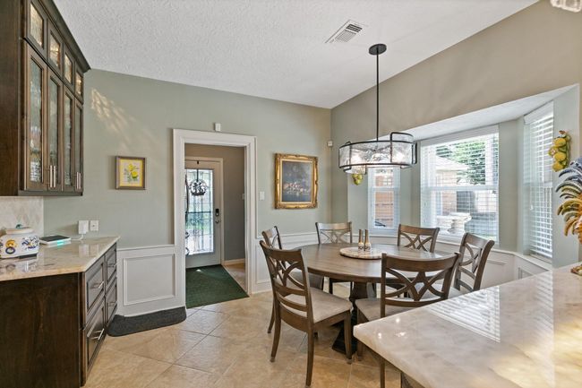 Charming breakfast room with bright windows and elegant lighting, perfectly positioned between the kitchen and back door for seamless indoor-outdoor entertaining. The convenient location makes it easy to serve poolside guests while enjoying casual meals in this inviting space. | Image 9