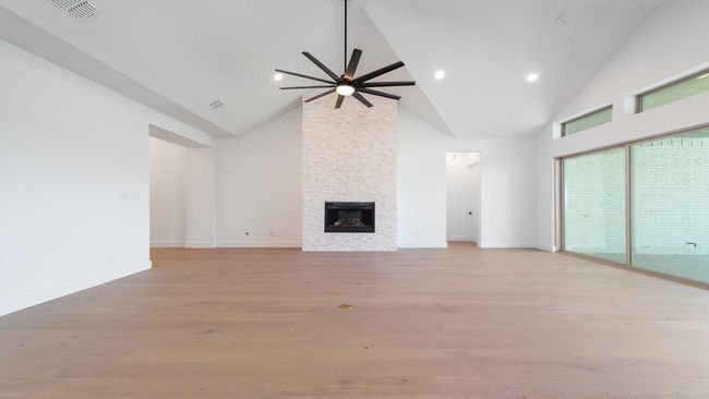 Unfurnished living room with a fireplace, high vaulted ceiling, ceiling fan, visible vents, and light wood-style flooring | Image 7